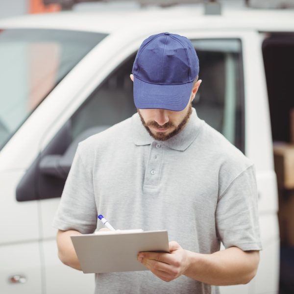 Delivery man writing on clipboard in front of his van